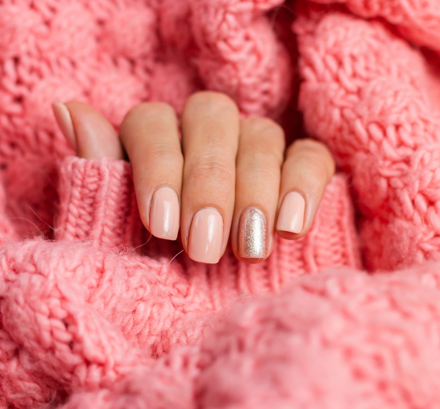 Pretty nude color manicure, one finger shiny golden, on knitted pink wool pillover background