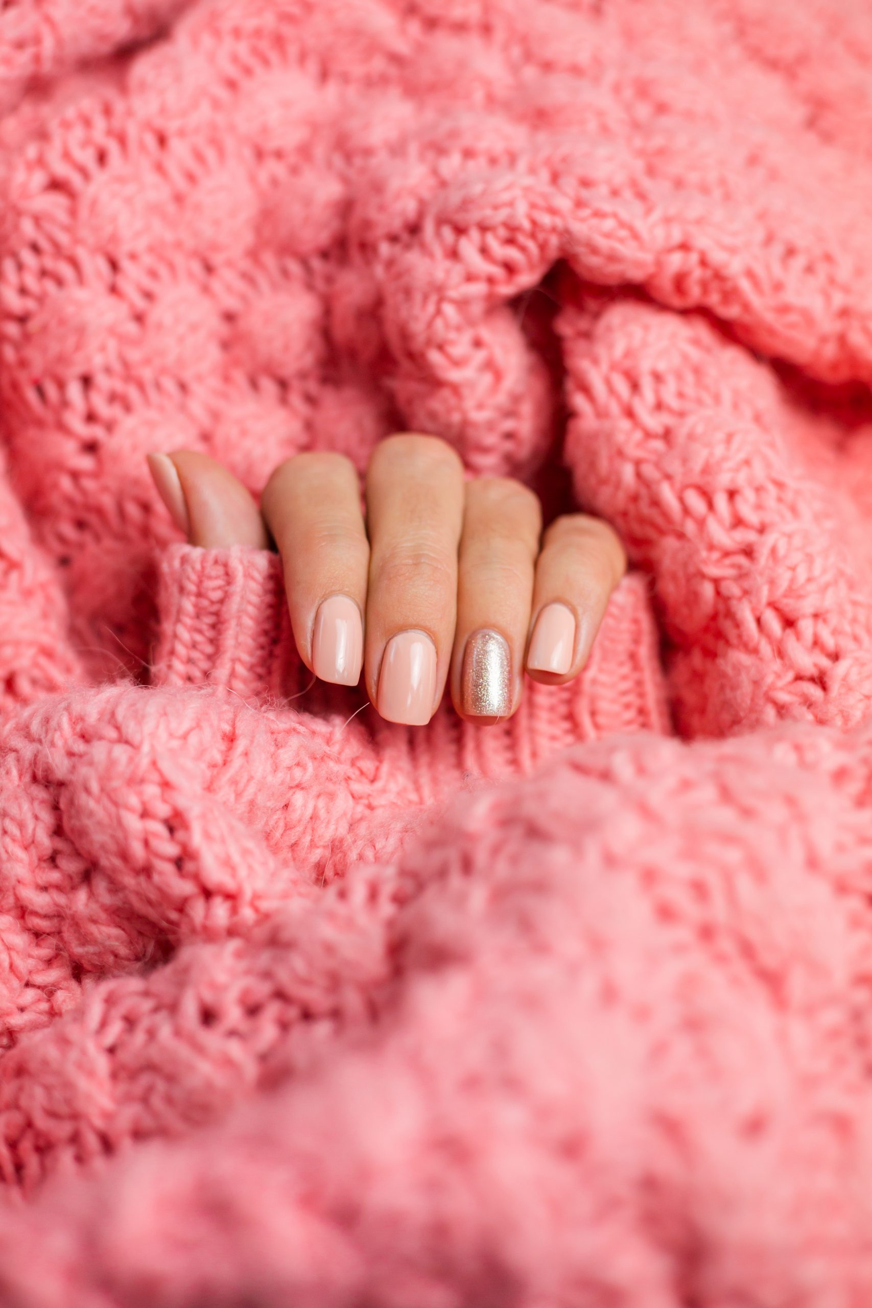 Pretty nude color manicure, one finger shiny golden, on knitted pink wool pillover background